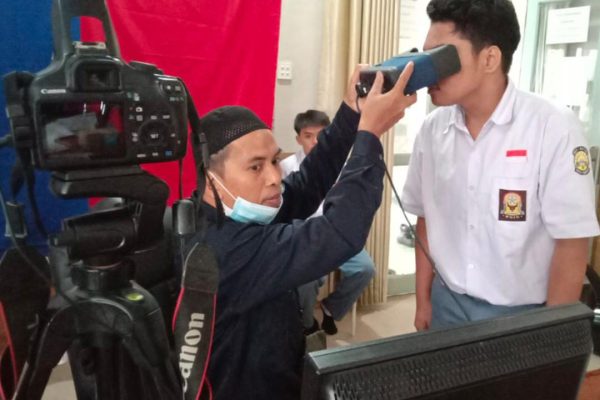 Petugas Disdukcapil melakukan perekaman biometrik terhadap seorang pelajar dalam pelayanan jemput bola KTP elektronik di sekolah. Program ini memudahkan pelajar melakukan perekaman tanpa harus datang ke kantor Disdukcapil.