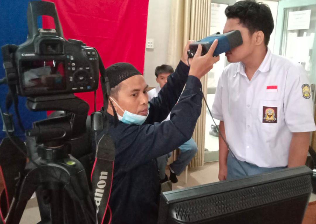 Petugas Disdukcapil melakukan perekaman biometrik terhadap seorang pelajar dalam pelayanan jemput bola KTP elektronik di sekolah. Program ini memudahkan pelajar melakukan perekaman tanpa harus datang ke kantor Disdukcapil.